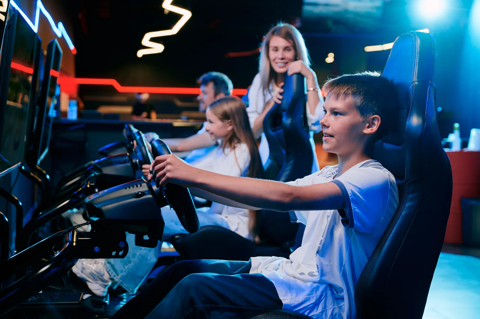 A boy at the wheel of a racing simulator, his family in the seats nearby