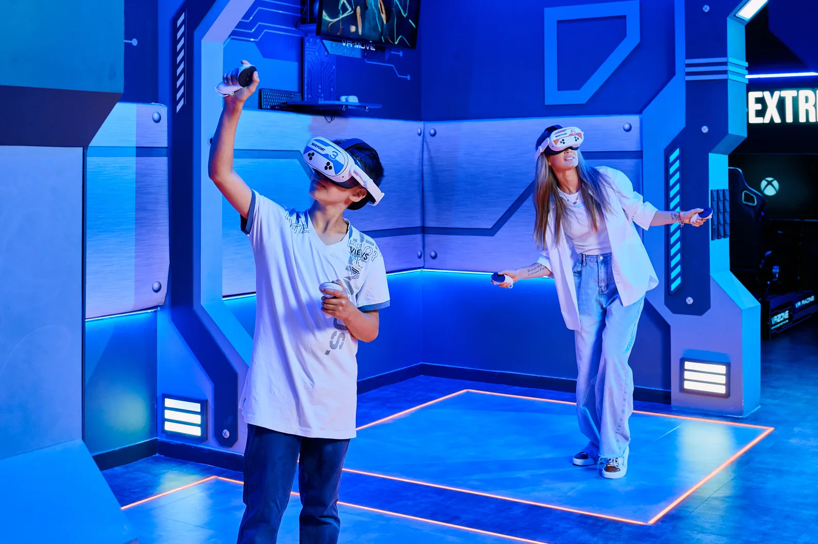 A mother and son in VR headsets play at the VR Station with lit zones on the floor